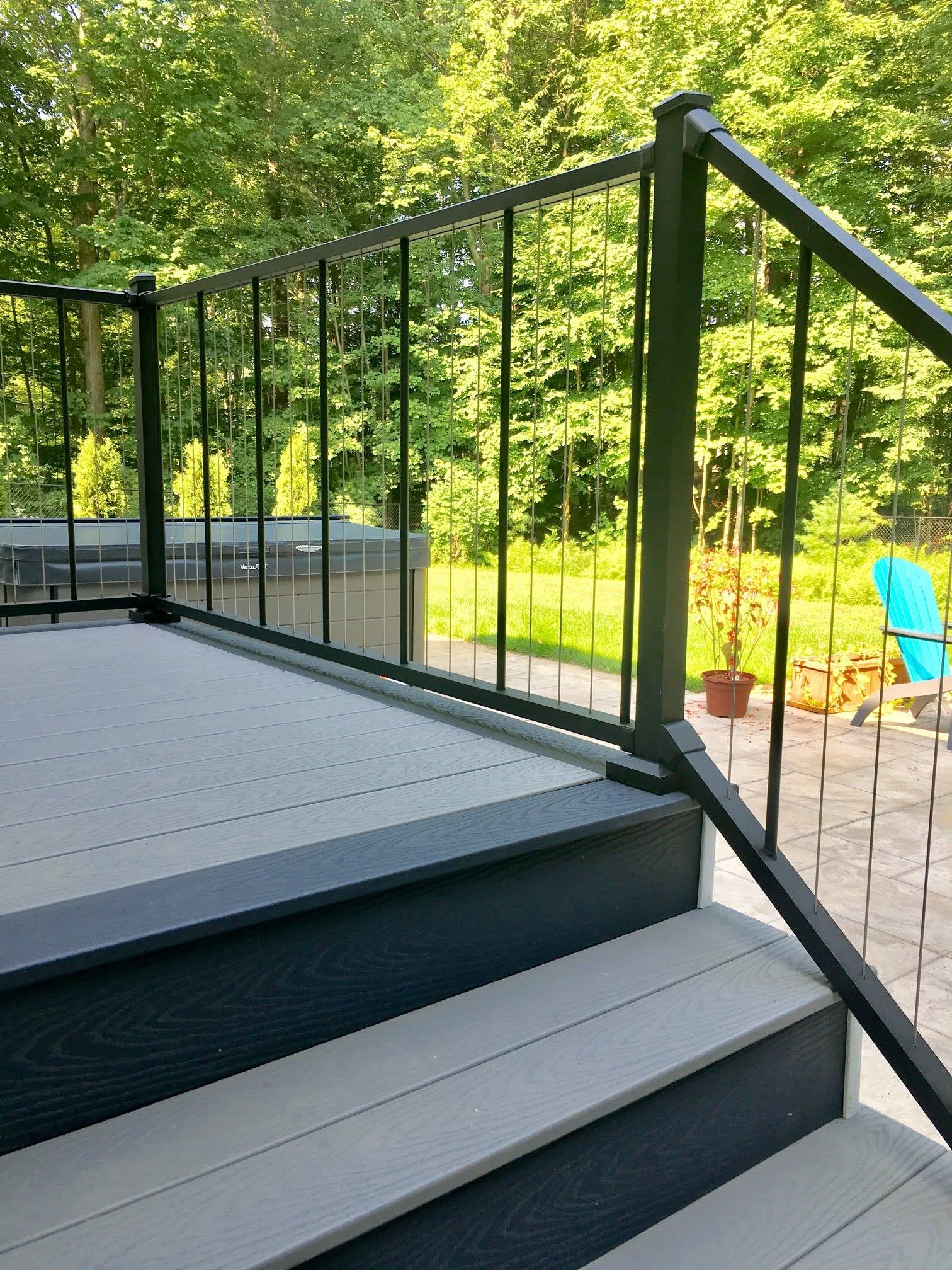 Composite deck steps with black aluminum rail above a stamped concrete patio