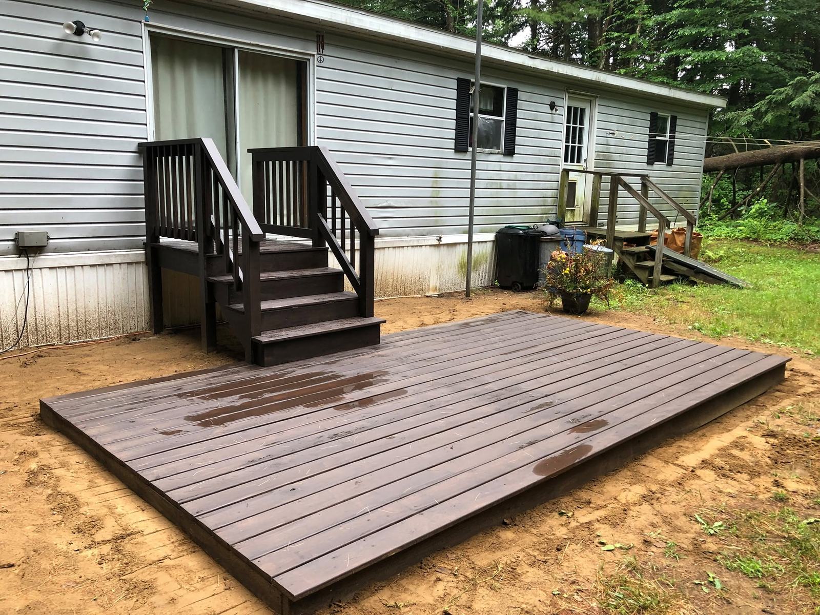 Dark-stained ground-level deck with entry steps beside a house